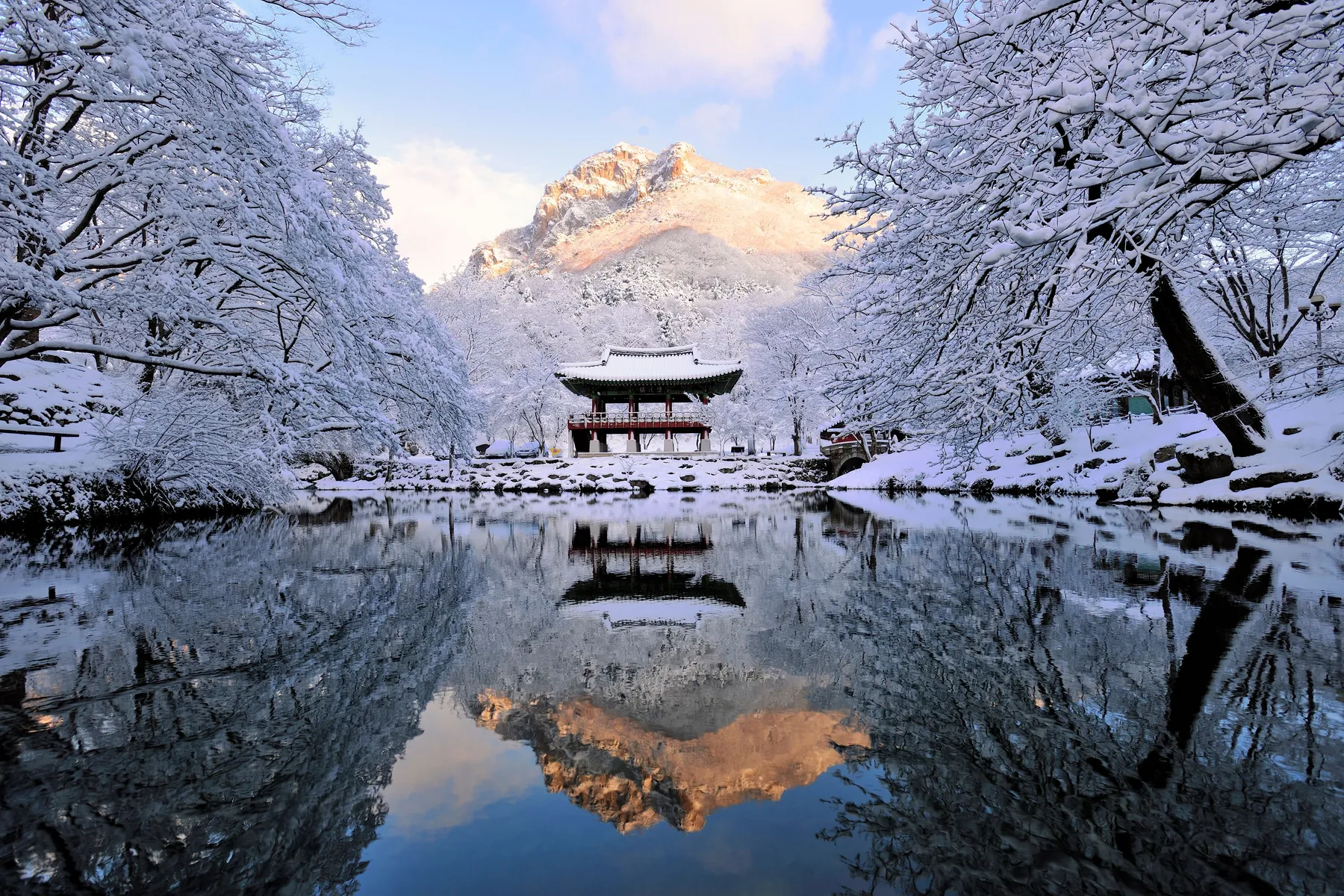 Baekhakbong peak glowing at sunrise above a snow covered temple pavilion at Baekyangsa